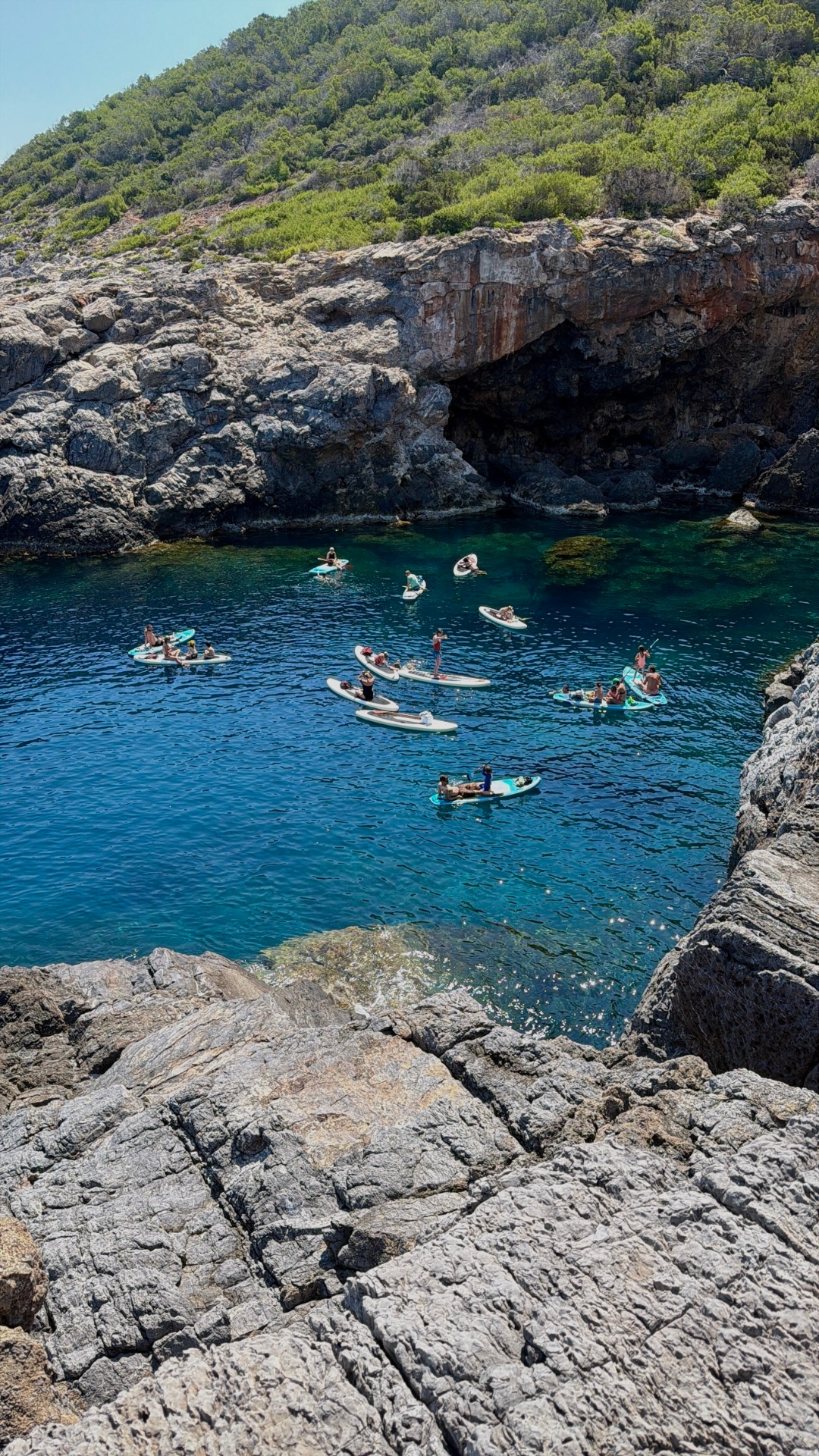 Paddleboarders gathered by a sea cave in a blue cove