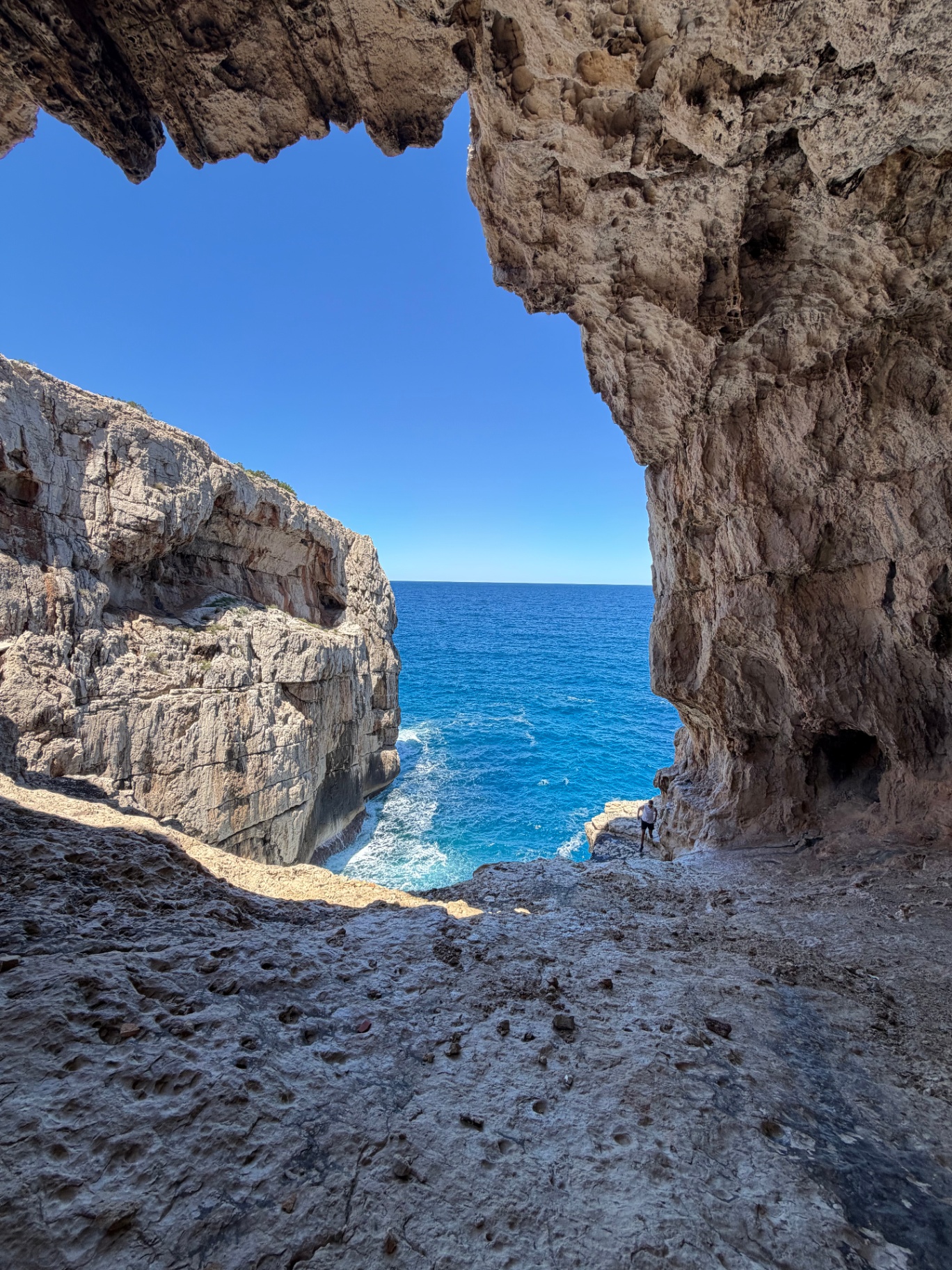 Jurassic Cave, hiker silhouetted in a massive cave opening above the turquoise sea